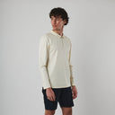 Man wearing a cream long-sleeve polo shirt and black shorts on a light gray background