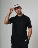 Man wearing a black outfit with a white cap on a gray background