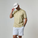 Man wearing a beige polo shirt and light gray shorts with a white cap on a plain background