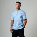 Man wearing a light blue polo shirt and black shorts against a gray background