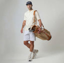 Man holding a tan golf bag against a plain background