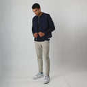 Man wearing a navy bomber jacket, light gray pants, and white sneakers on a plain background